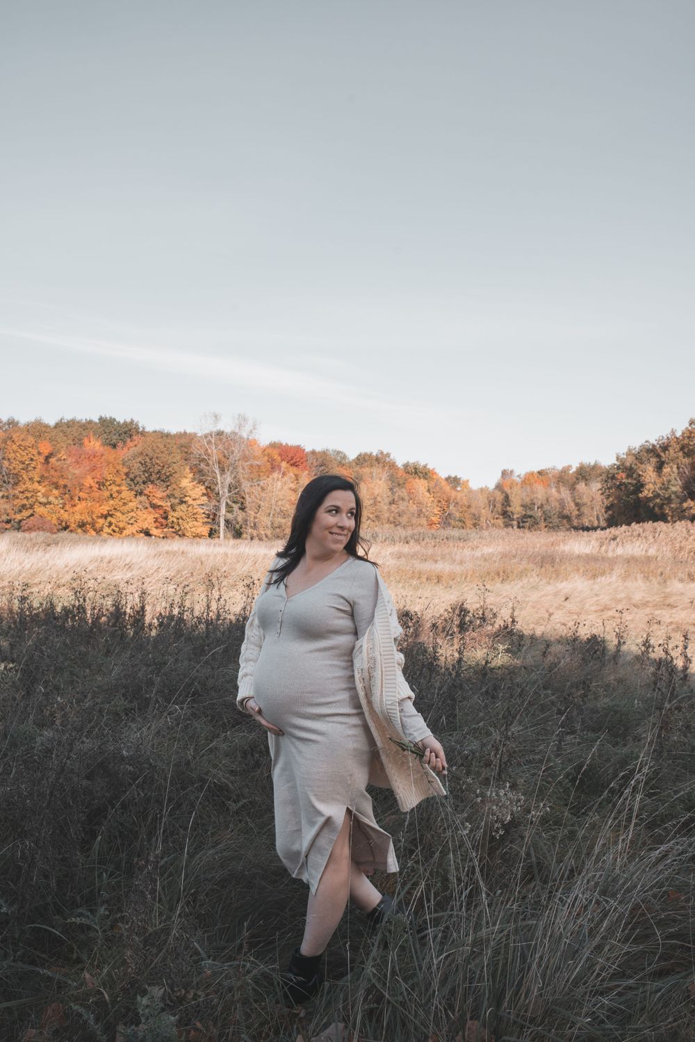 Woman in sweater walking through tall grass during autumn sunset.