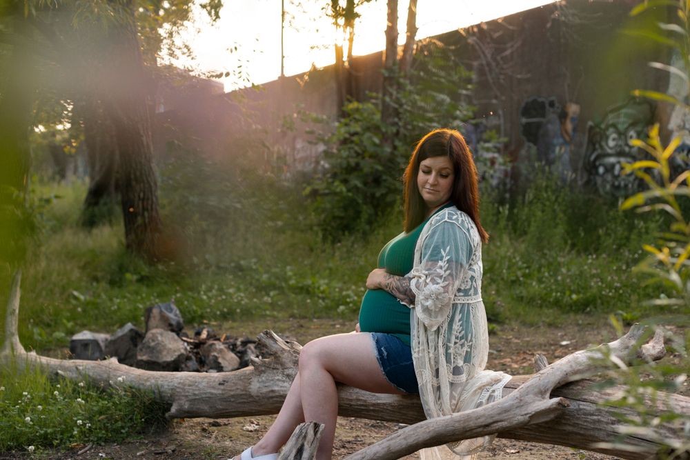Maternity photoshoot in natural setting with sunlight filtering through trees.