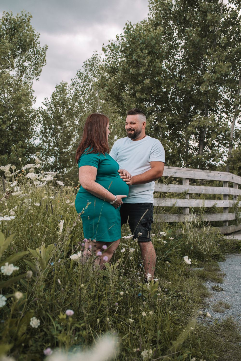 Couple embracing in a natural outdoor setting with wildflowers and wooden fence.