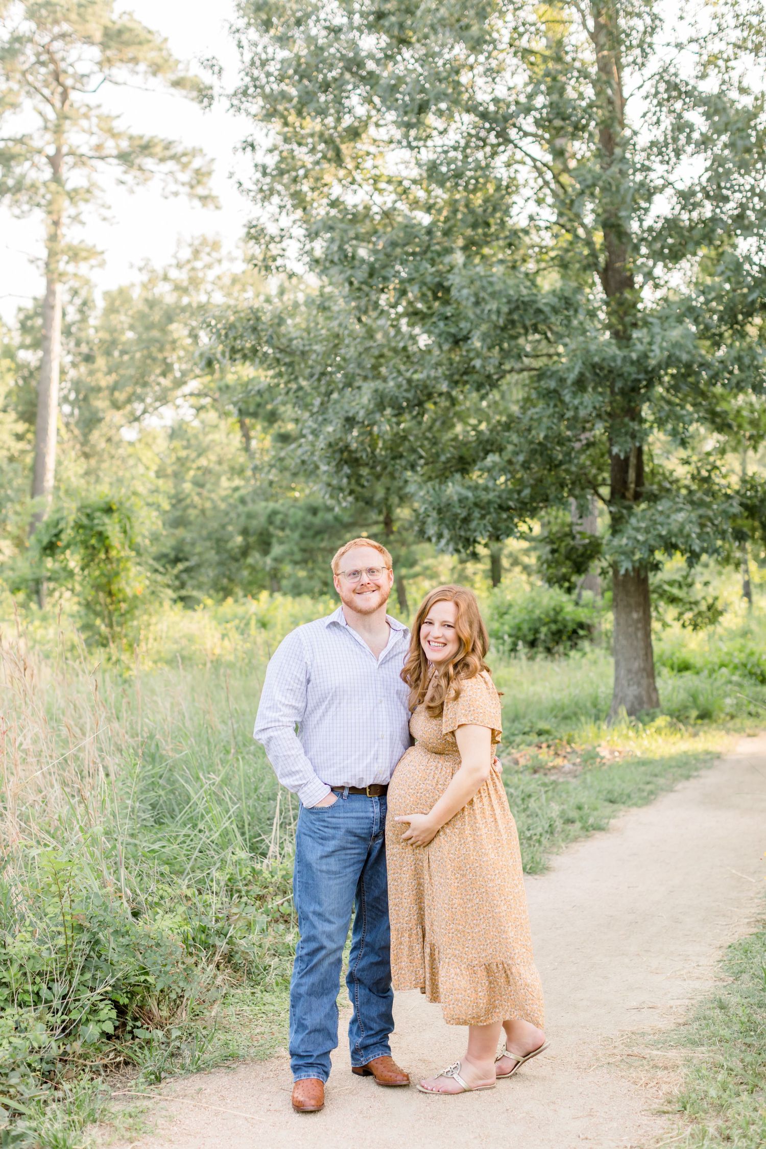 Expecting couple stands together on forest path during sunset photo session.