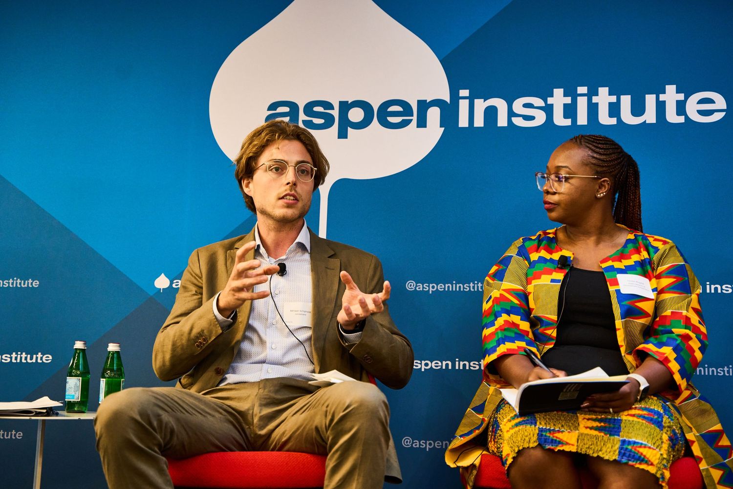 Speakers engaged in discussion during an Aspen Institute panel event with blue backdrop.