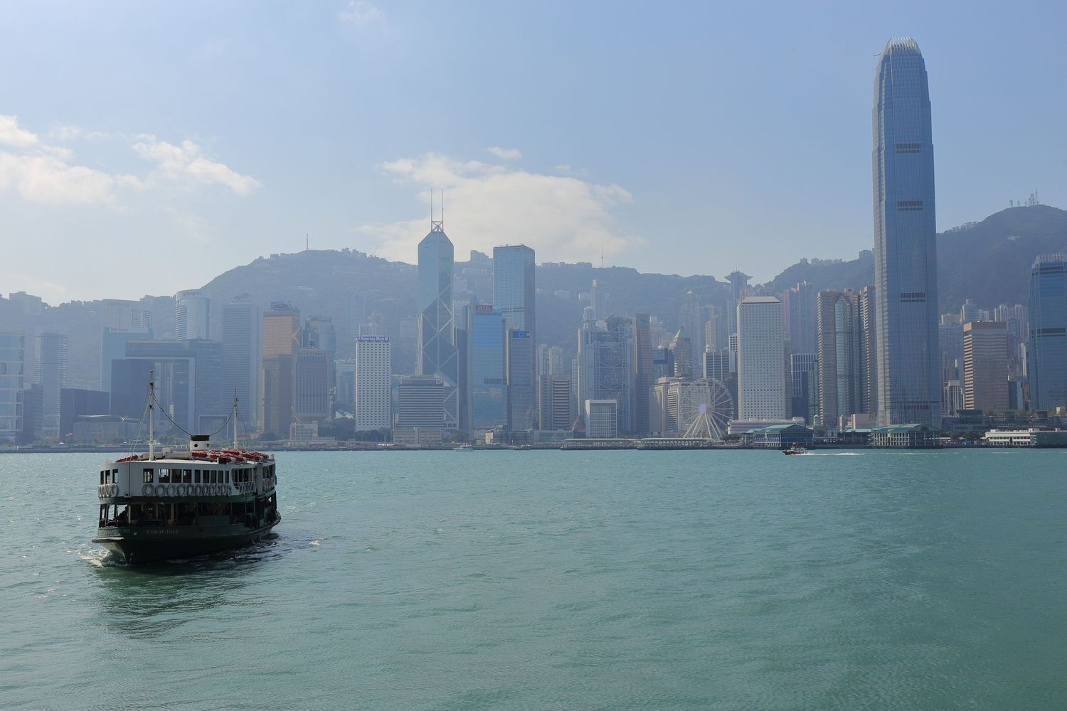 Traditional junk boat crossing Victoria Harbor with Hong Kong's modern skyline backdrop.