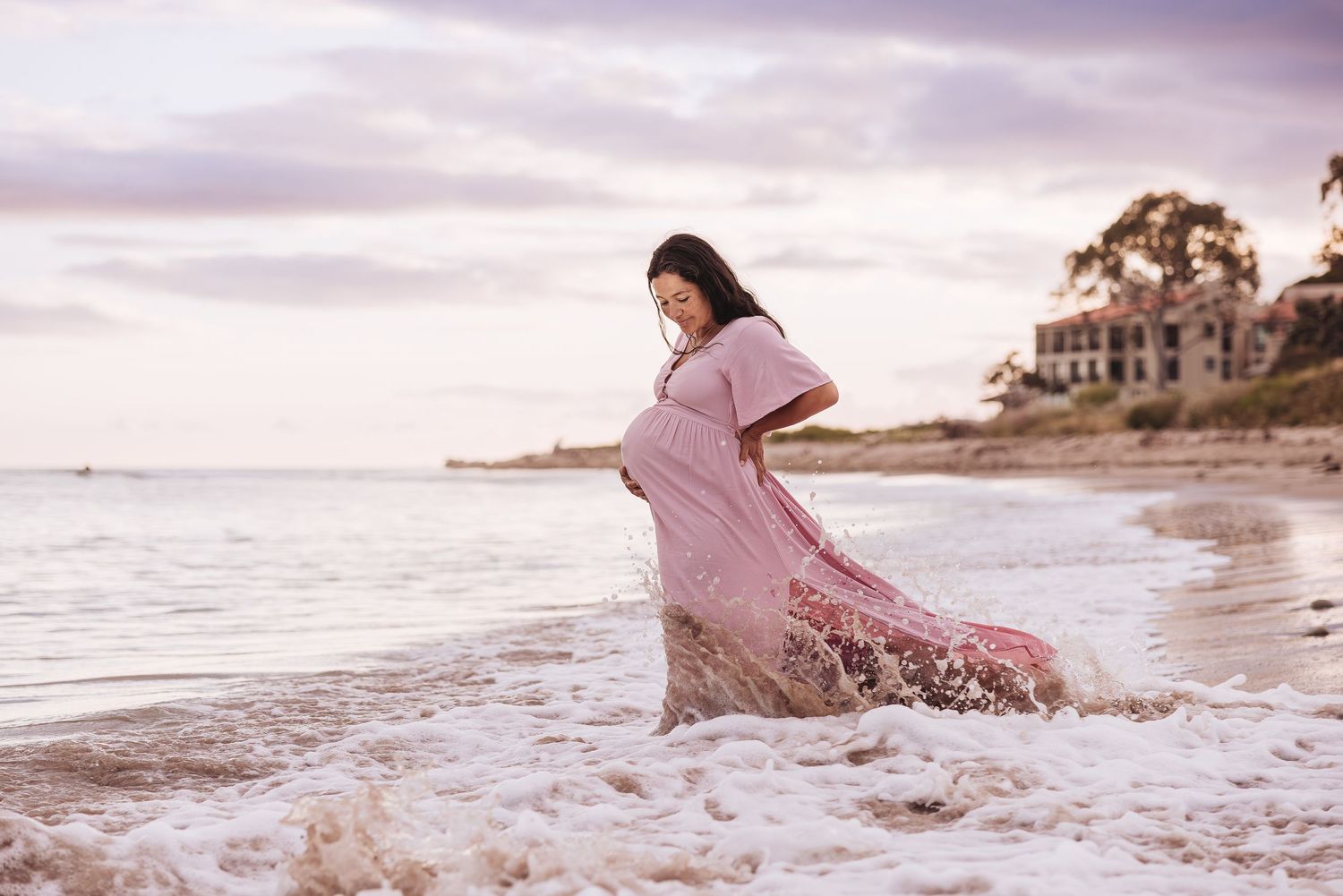 Pregnant woman standing in the water at the beach in Santa Barbara holding her belly.