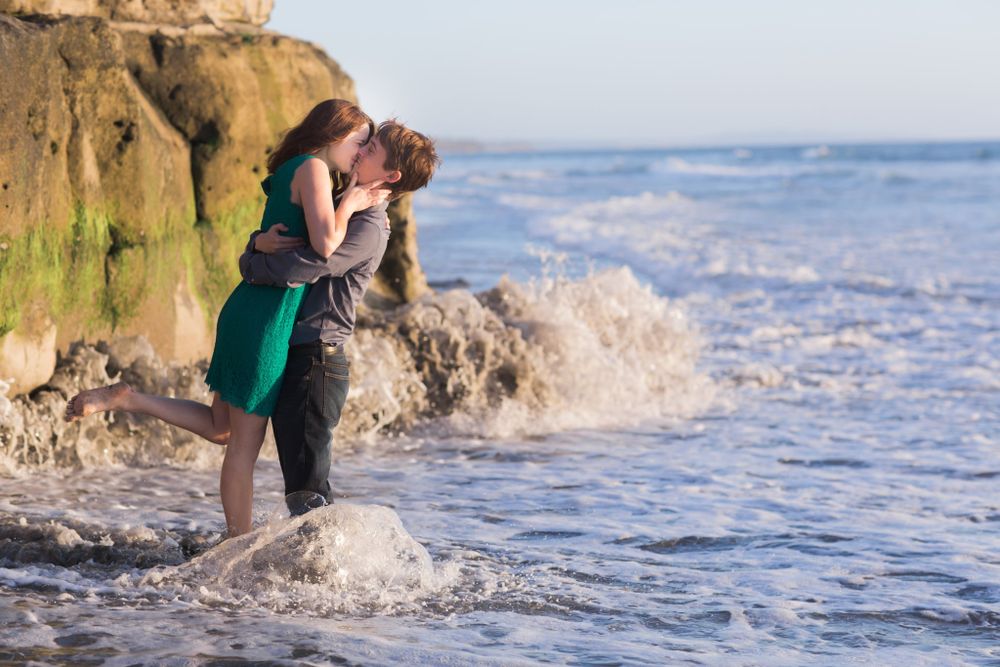 A couple shares a romantic moment on rocky cliffs by crashing ocean waves.
