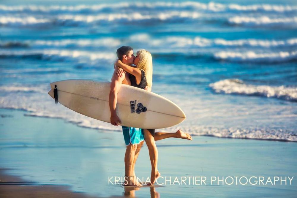 Person carrying white surfboard walking along beach with blue waves in the background.