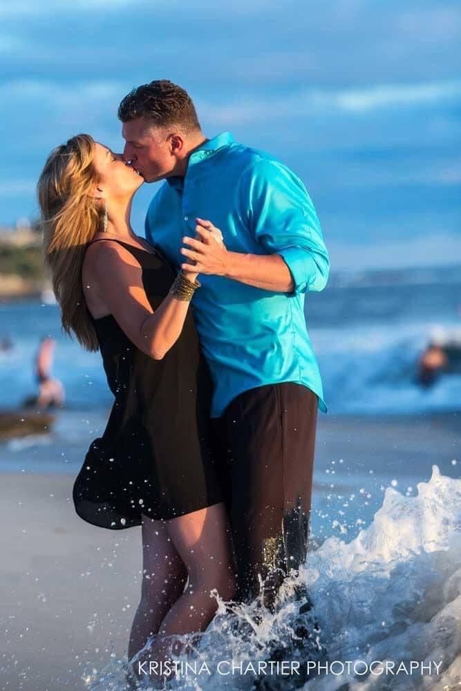 Romantic beach moment with crashing waves on a cloudy day.