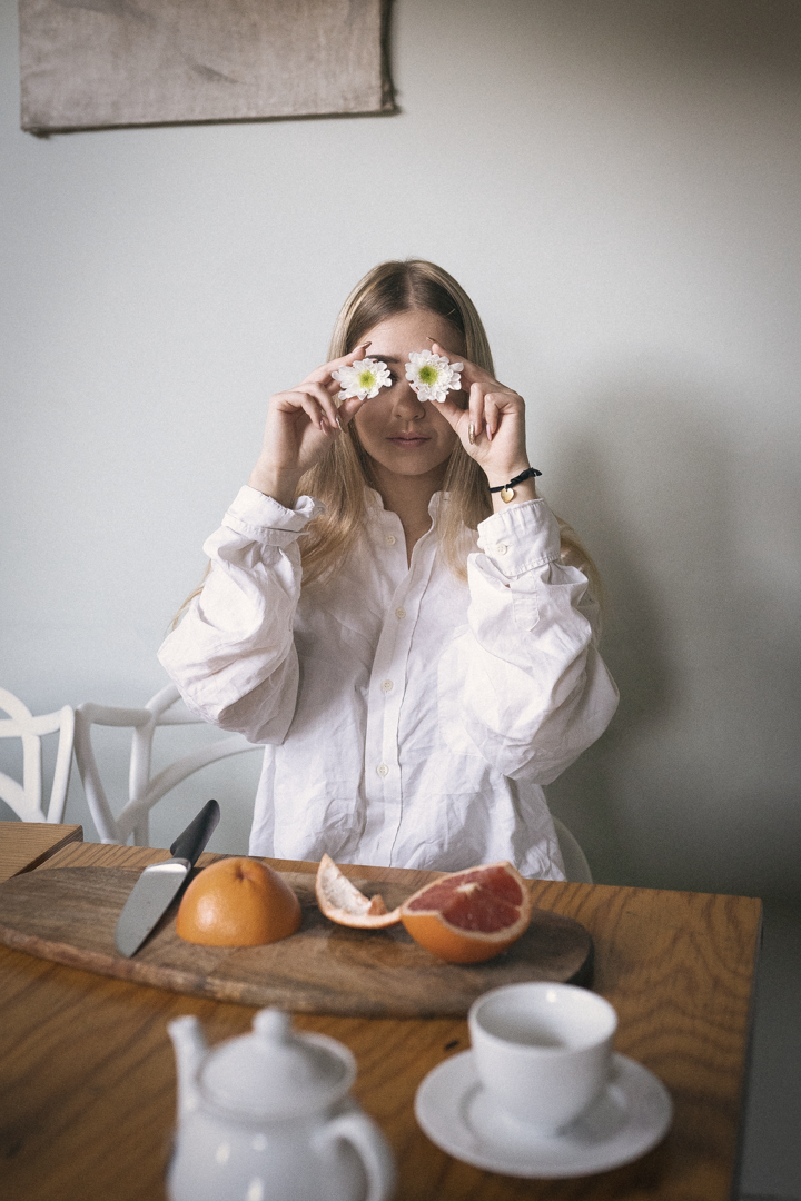 Creative breakfast scene with citrus fruit and person holding orange slices over eyes.