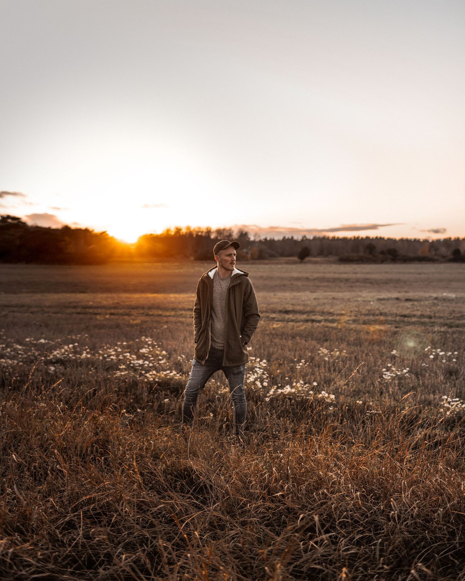 A silhouetted figure stands in a golden autumn field at sunset with mountains in the background.