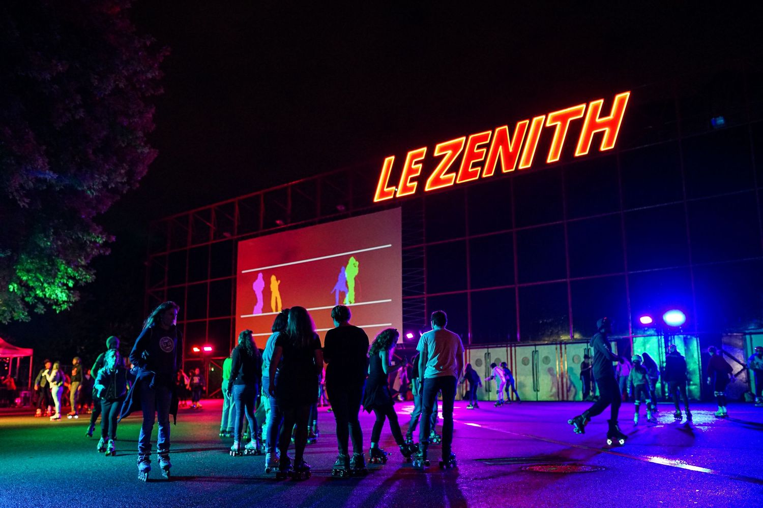 Illuminated Le Zenith concert venue sign at night with silhouetted crowd and colorful lighting in background.