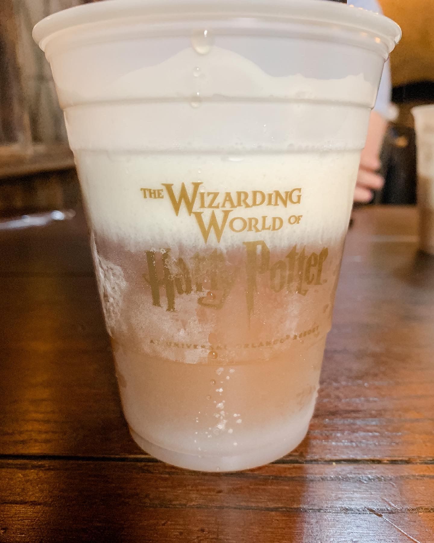 A Wizarding World branded beverage in a white disposable cup on a wooden table.