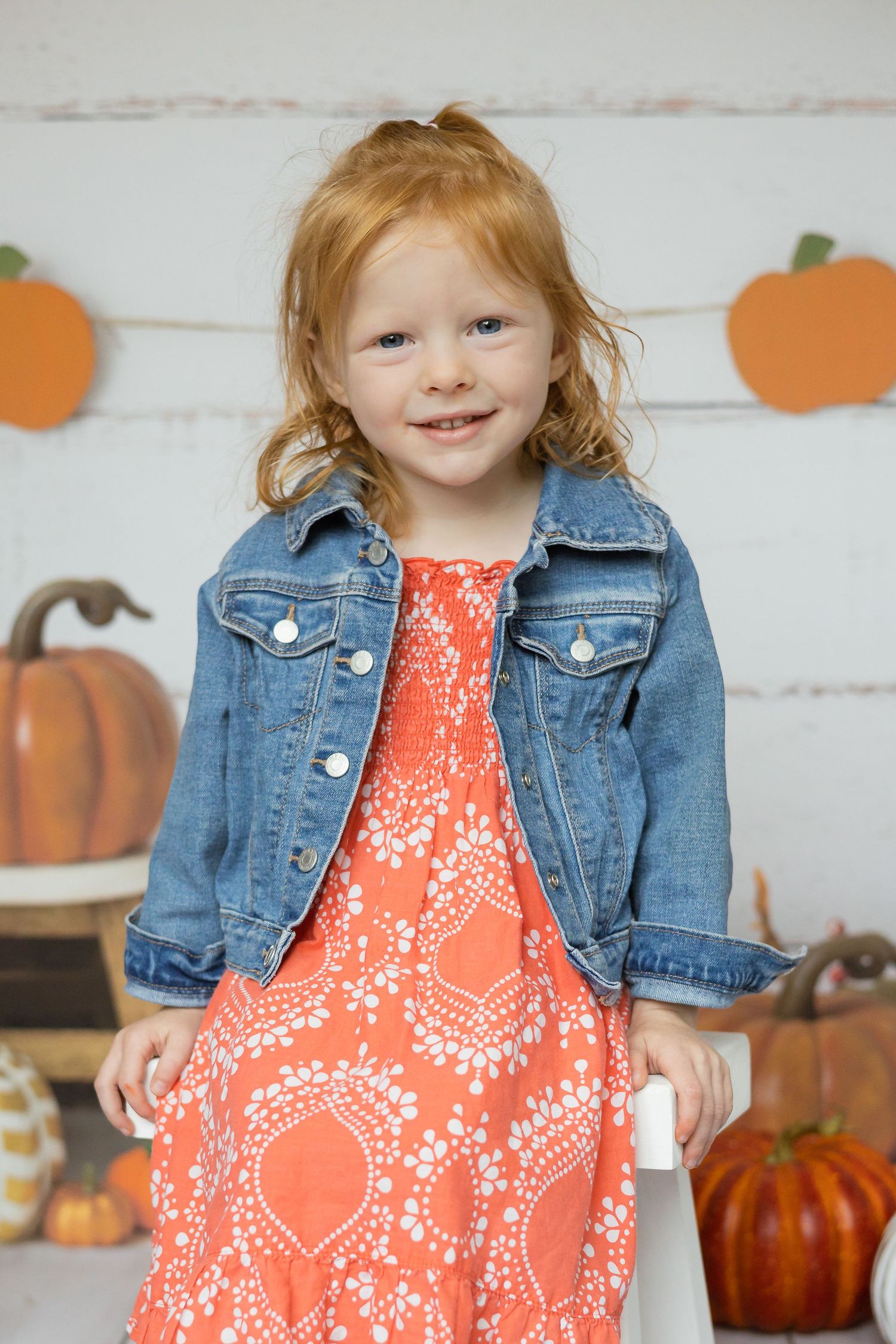 Young girl posing in a coral dress and jean jacket for fall school portraits