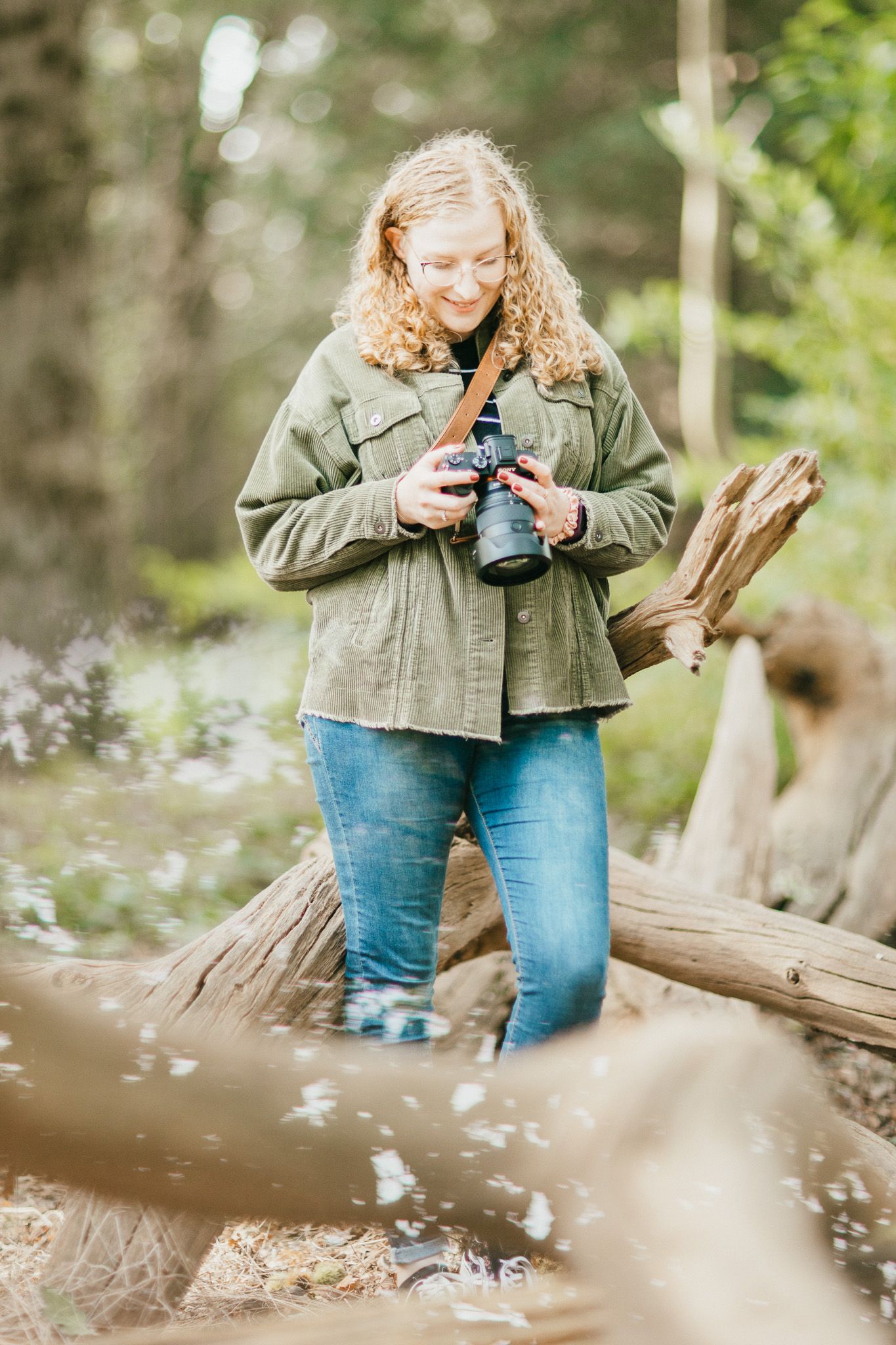 Nature photographer in casual outdoor wear holding camera while standing on fallen log.