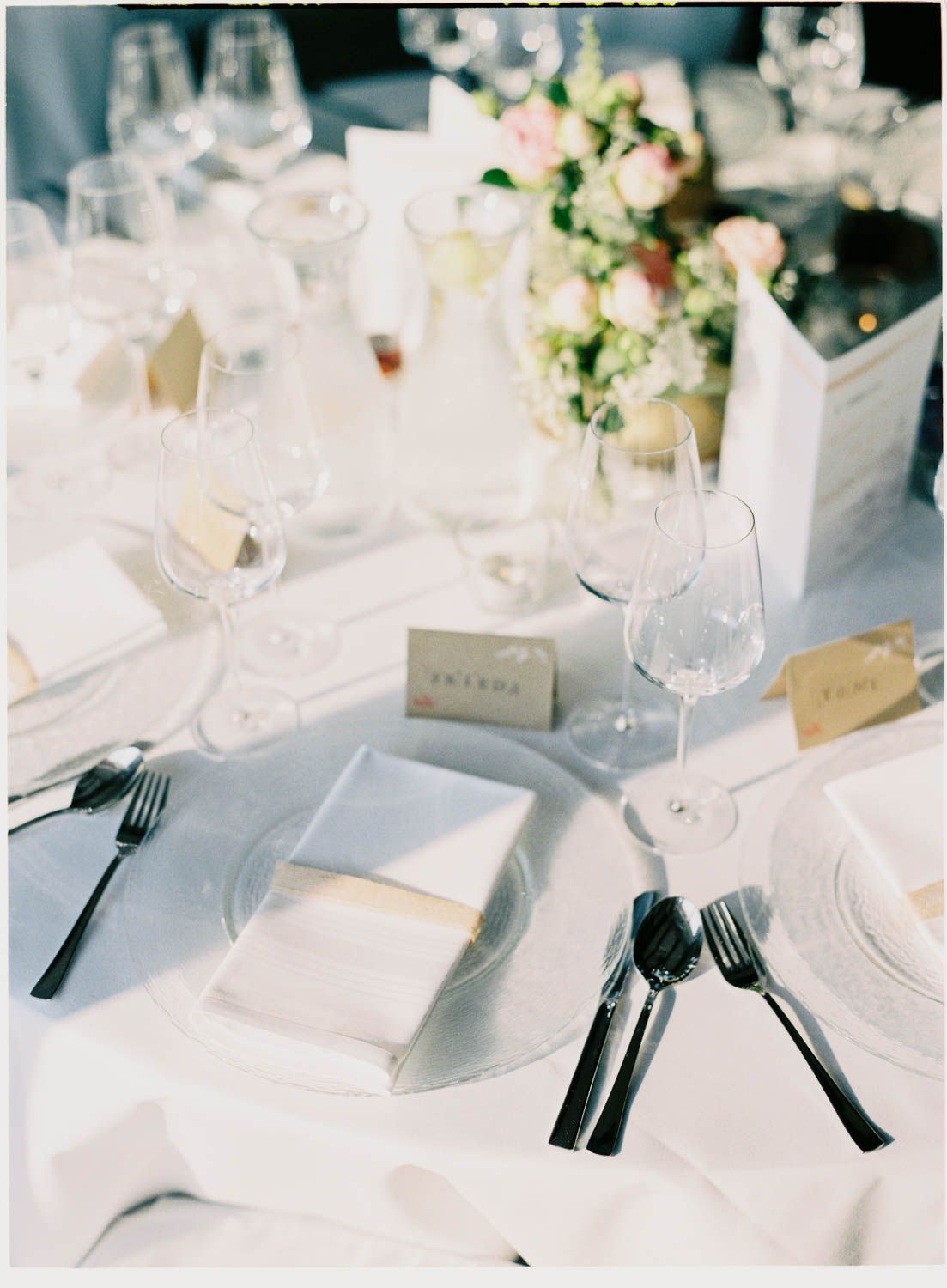Elegant wedding table setting with white linens, wine glasses, and delicate floral centerpieces.