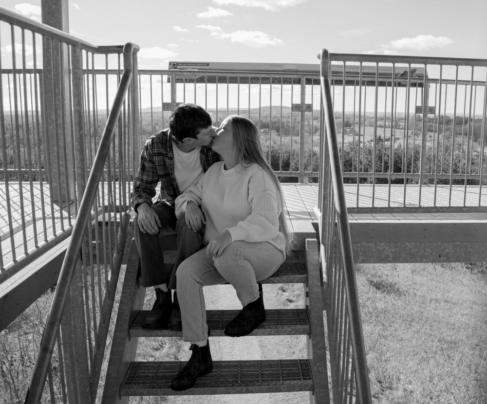 A romantic black and white photo of a couple sitting together on metal stairs outdoors.
