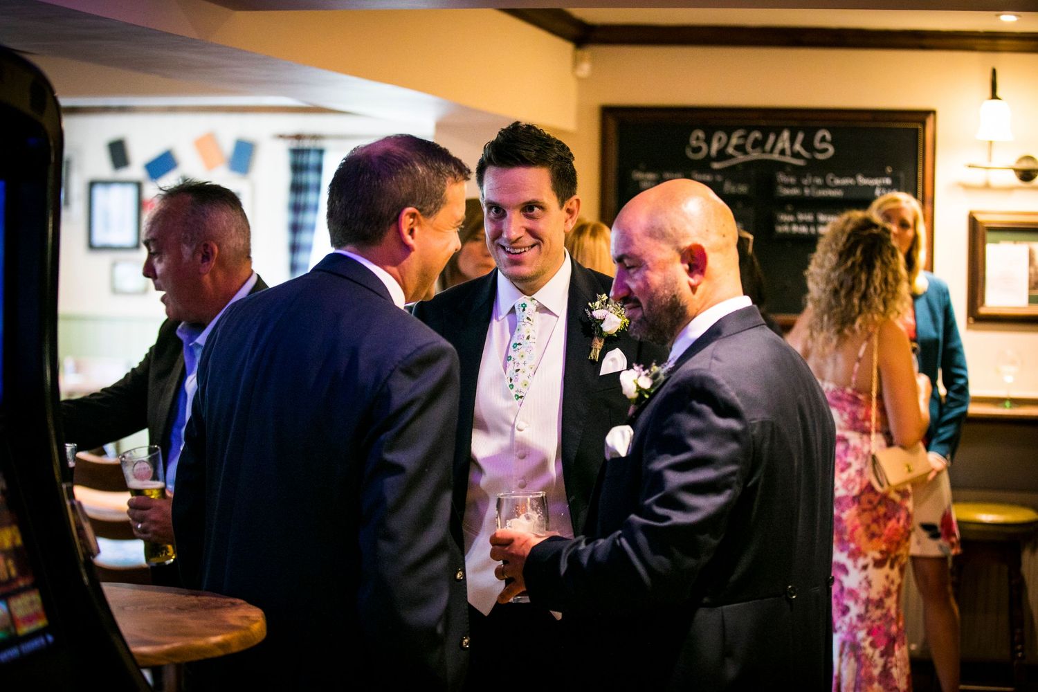 Guests mingle and socialize at an indoor reception venue with warm lighting and casual atmosphere.