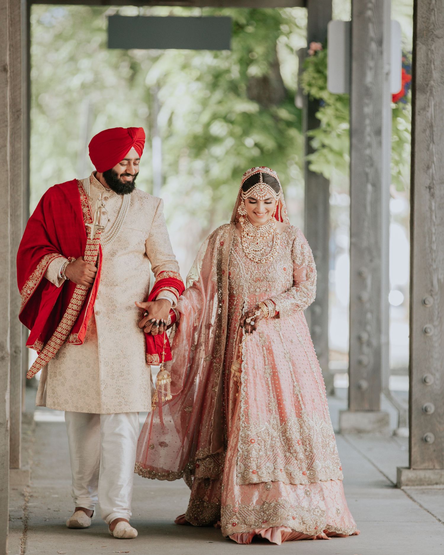 Sikh bride and groom walking together in traditional pink and cream embroidered wedding attire.