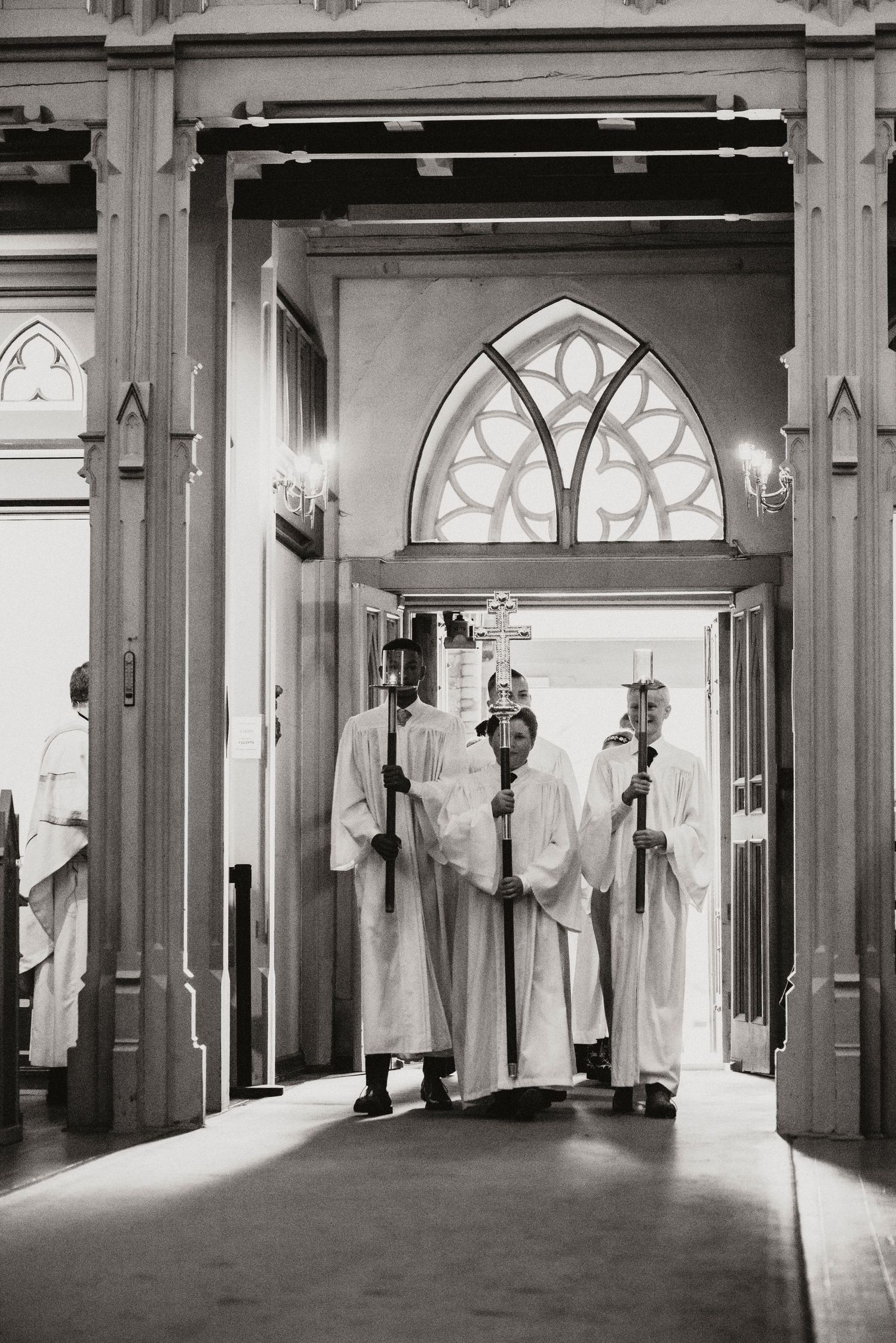Black and white photo of robed figures standing in a gothic church doorway with ornate architectural details.