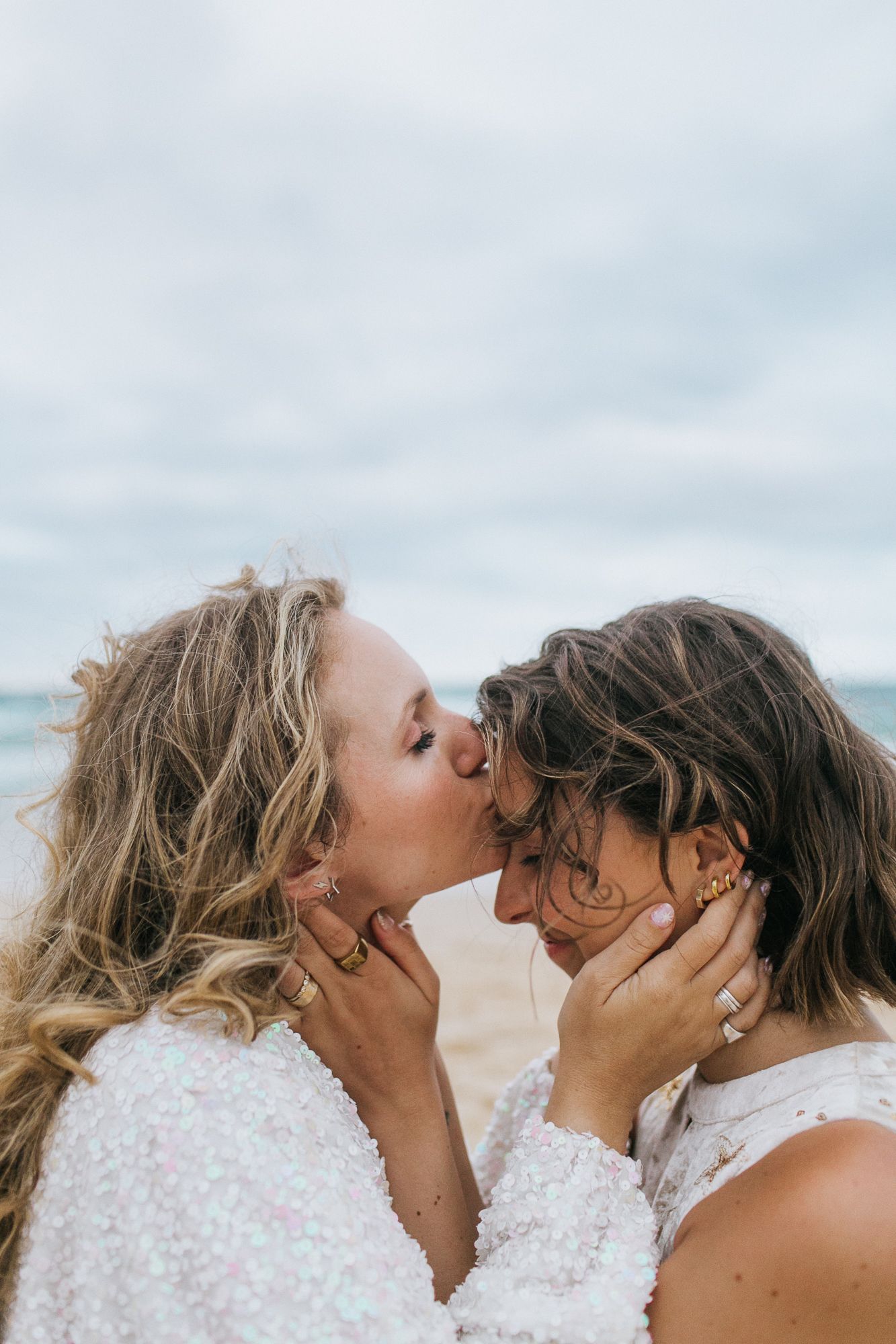 Two brides share a tender kiss on the beach on their wedding day.