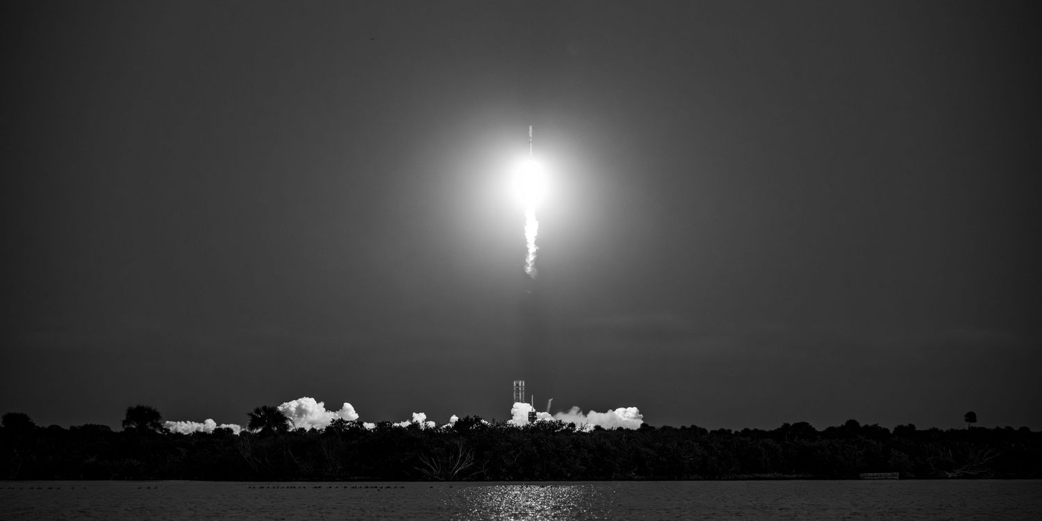 Night launch of a rocket with bright exhaust illuminating surrounding buildings.