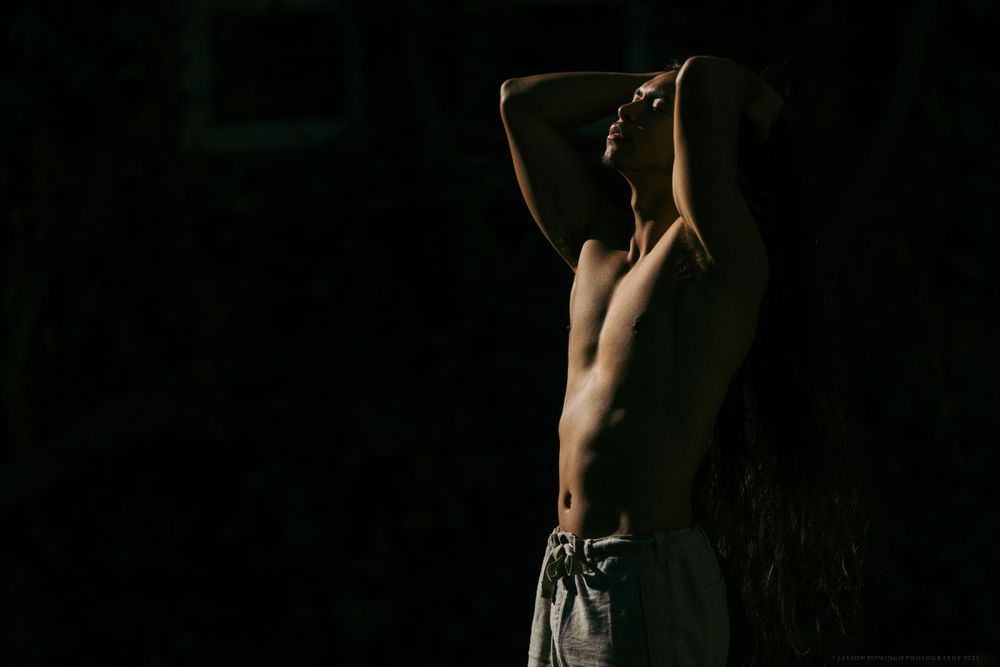 Dramatic shadowed portrait showing muscular torso against dark background.