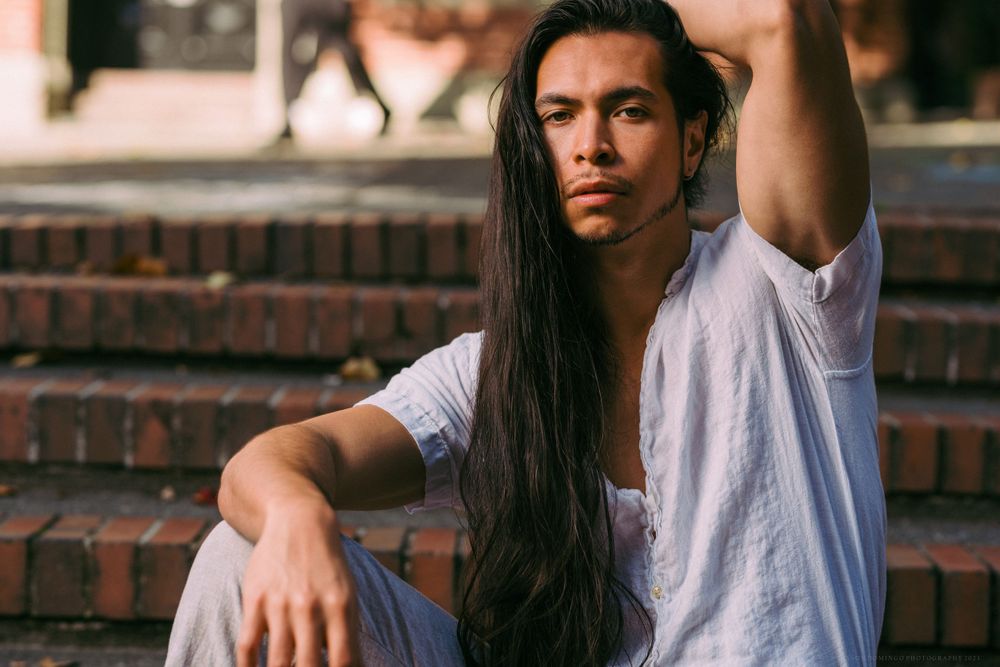 Casual portrait on brick steps with flowing long dark hair in white t-shirt.