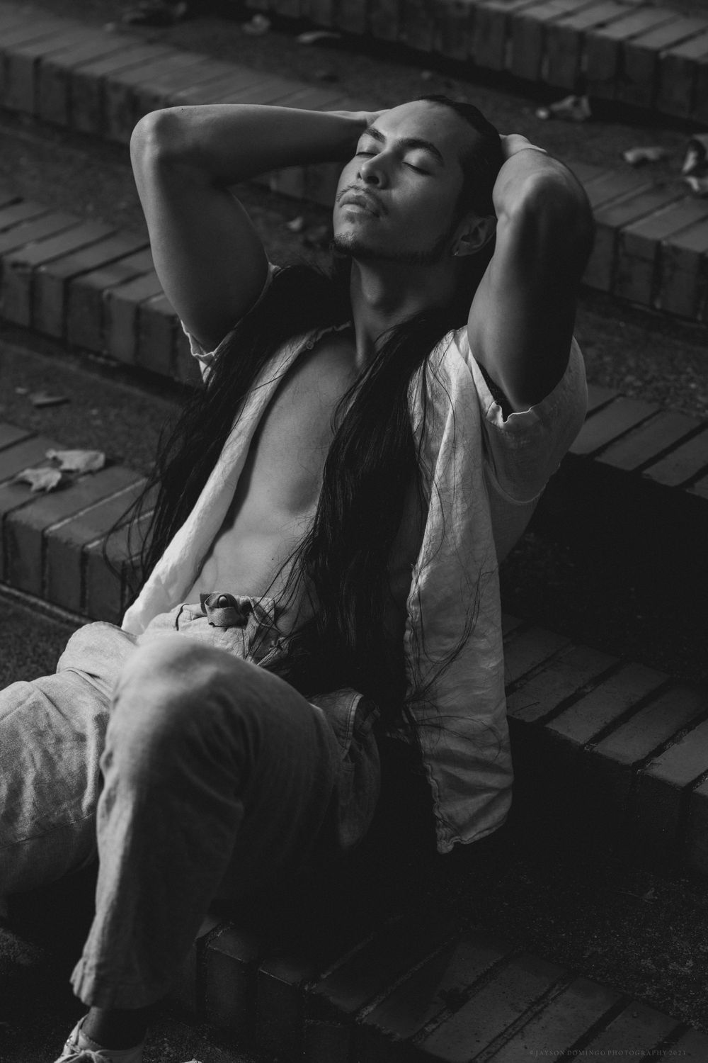 Dramatic black and white portrait of model reclining on steps with long hair.