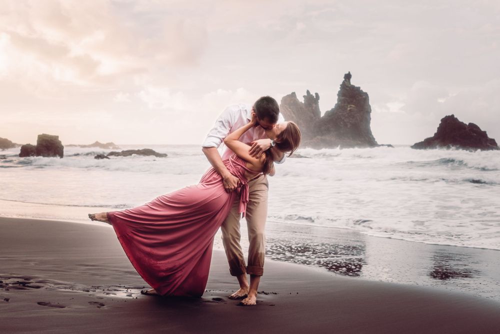 Man embracing and kissing his pregnant wife, wide angle shot of wild beach in Canary Islands.