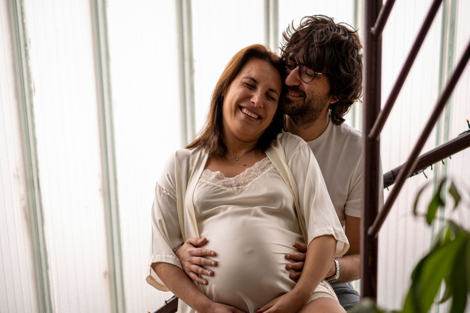 An expecting couple sharing a tender moment by a window.
