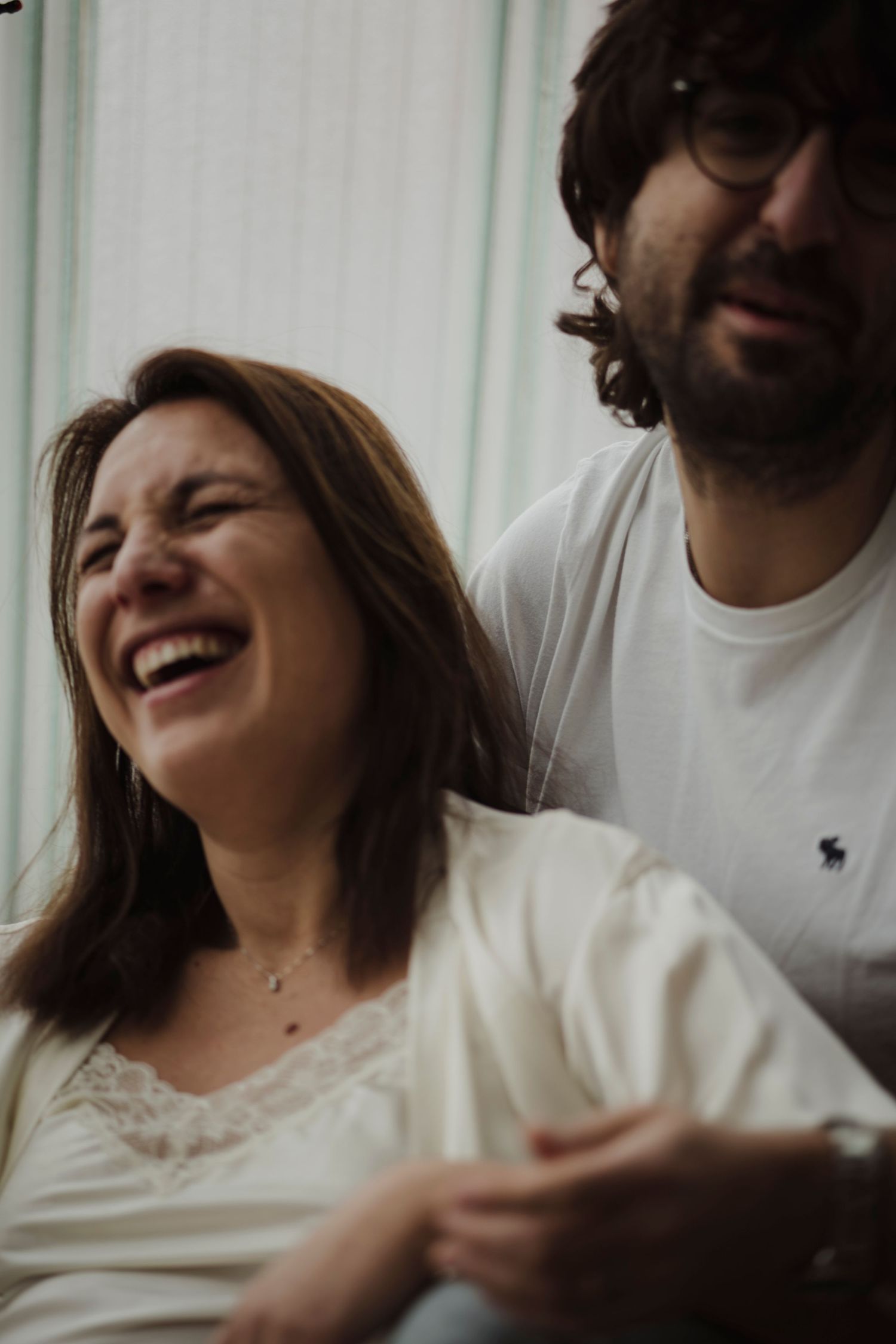Intimate couple sharing a joyful candid moment together while laughing in natural light by a window.