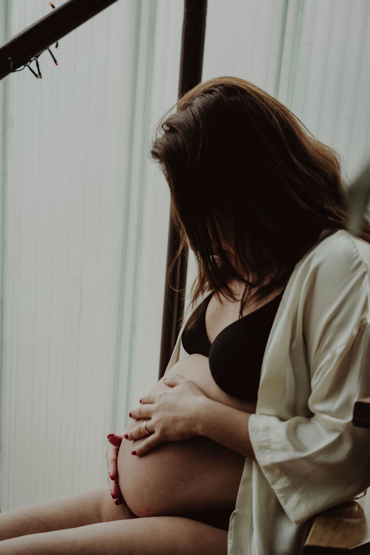 Side view of an expectant mother in white cardigan touching her pregnant belly.