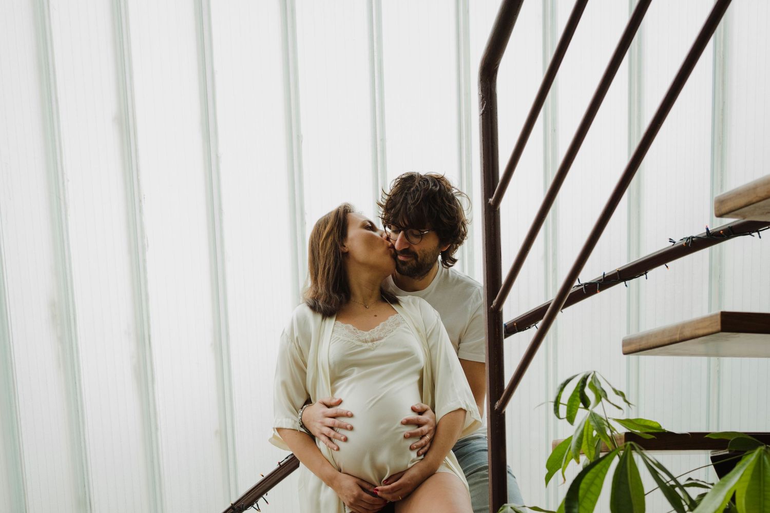 Expecting couple embracing on wooden staircase during intimate maternity photoshoot.