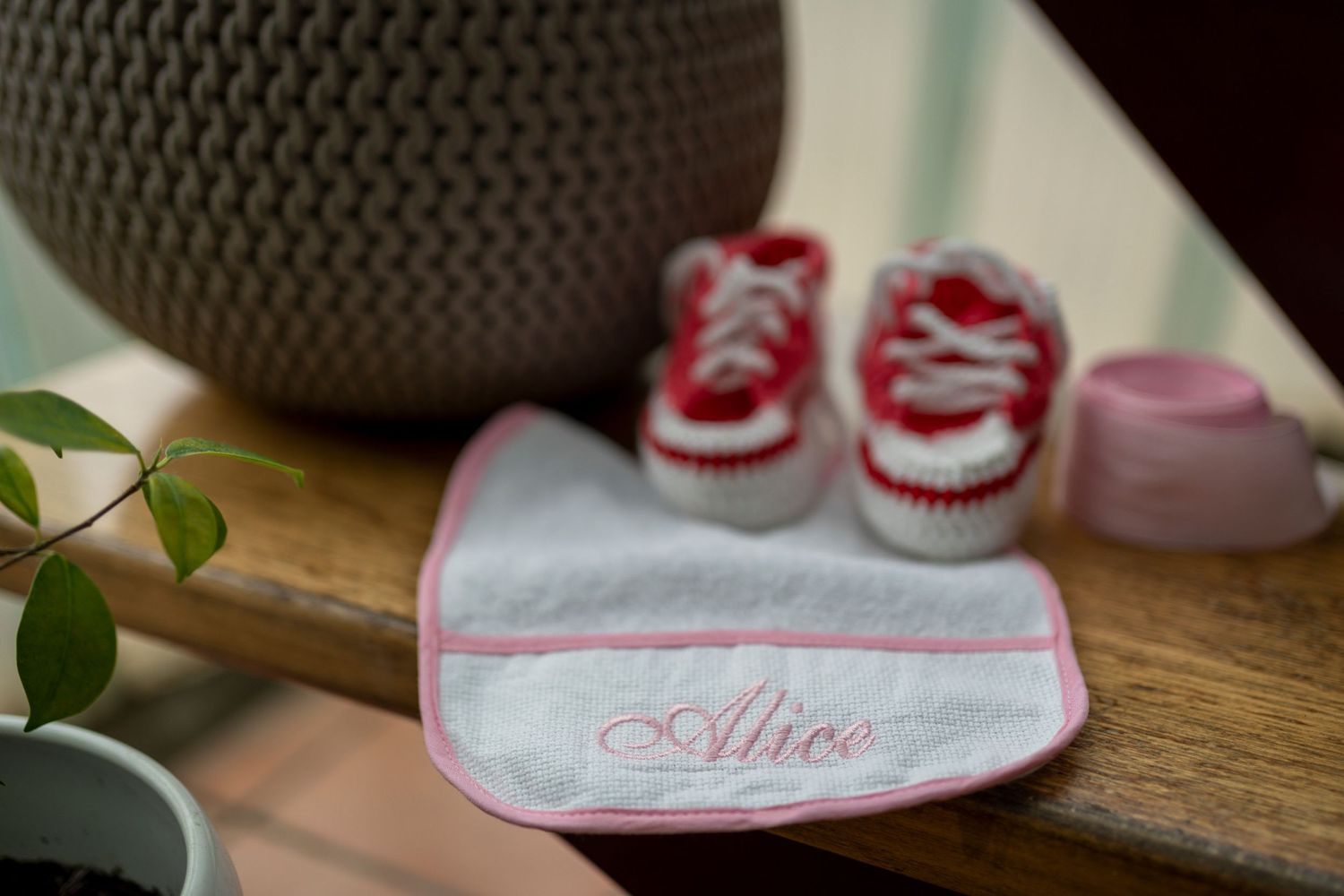 A personalized pink and white baby bib with tiny red baby sneakers displayed on a wooden surface.