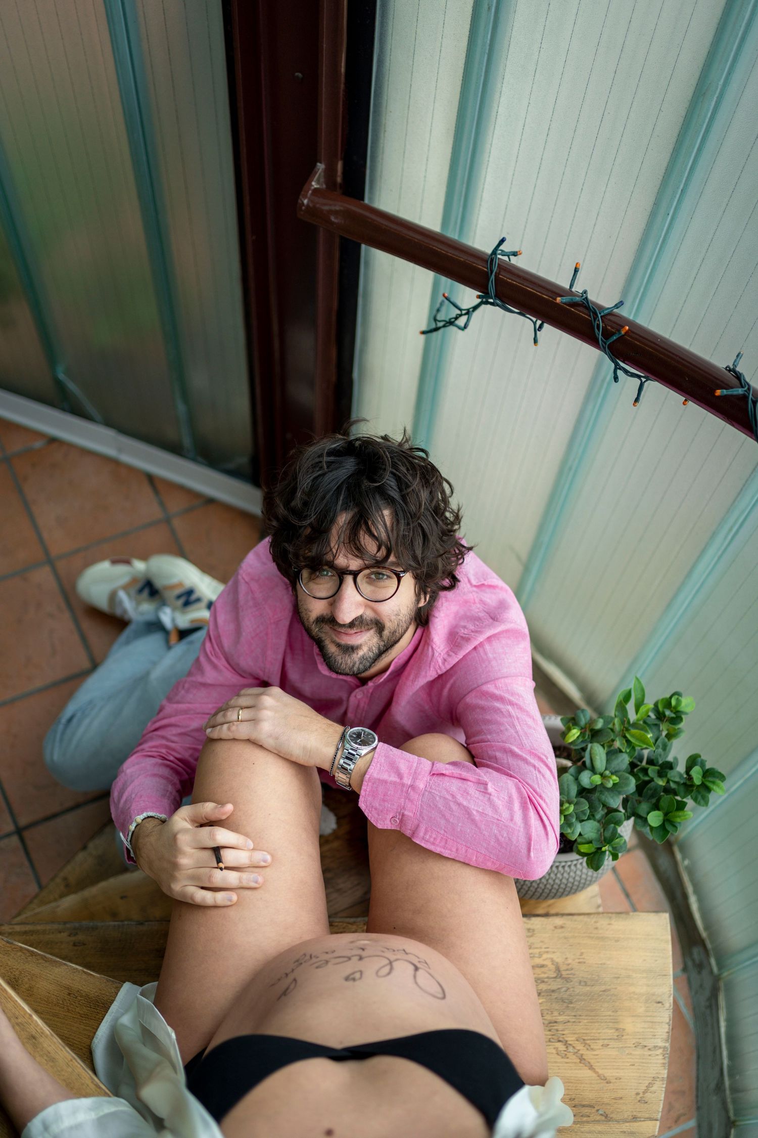 Person in glasses and pink sweater drawing on pregnant belly near indoor plants.