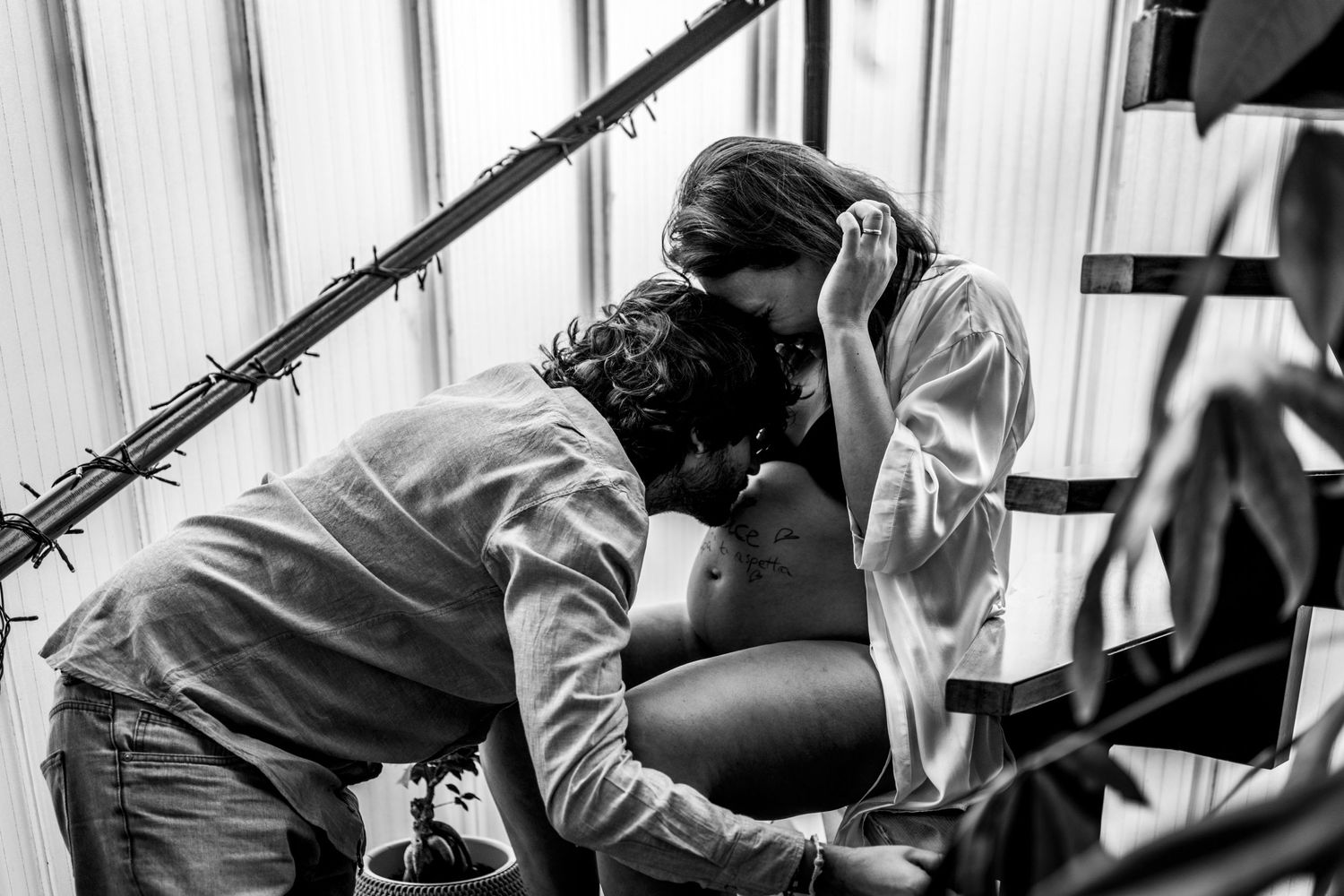 Black and white intimate maternity moment captured near window.