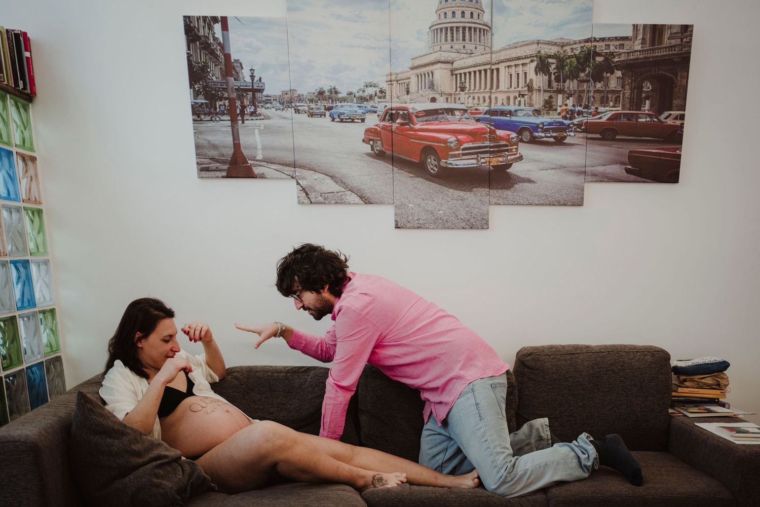 Maternity photo session in living room with vintage Havana artwork on wall.