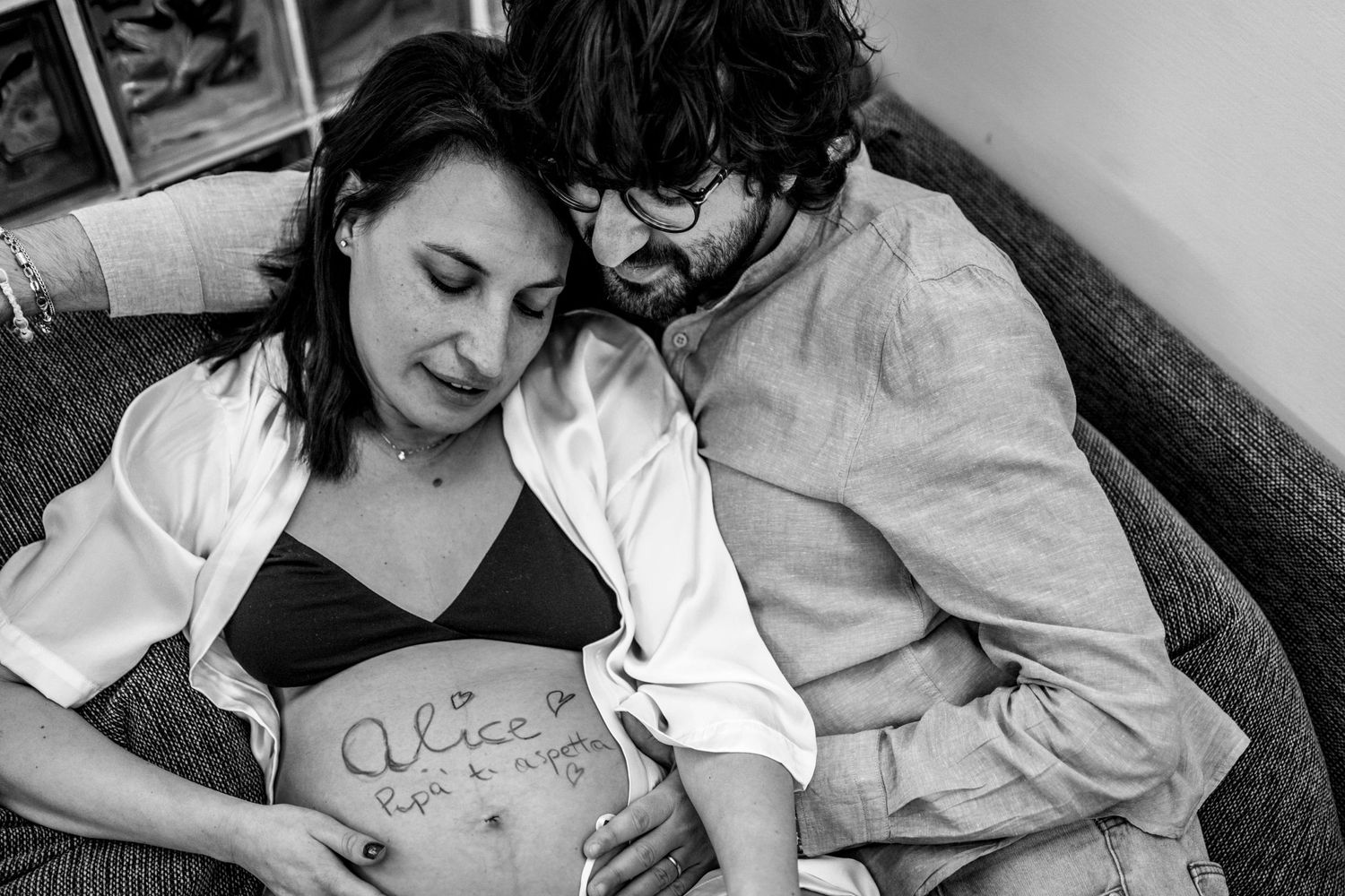Black and white photo of a tender pregnancy moment with handwritten belly art.