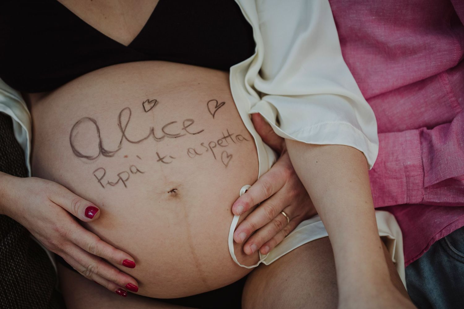 Close-up of pregnant belly with handwritten name and hearts.