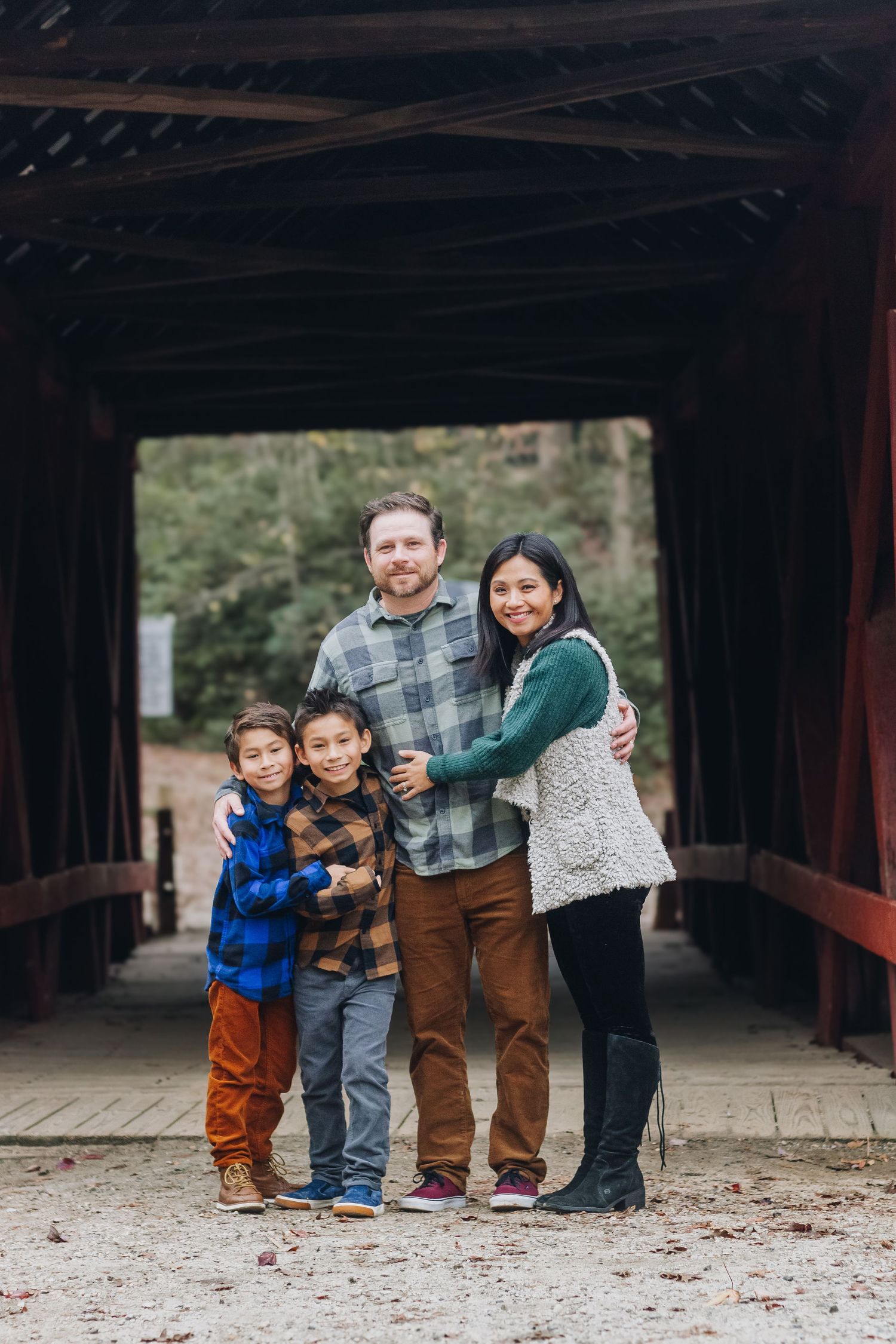 Family of four poses together under covered bridge during outdoor photo session.