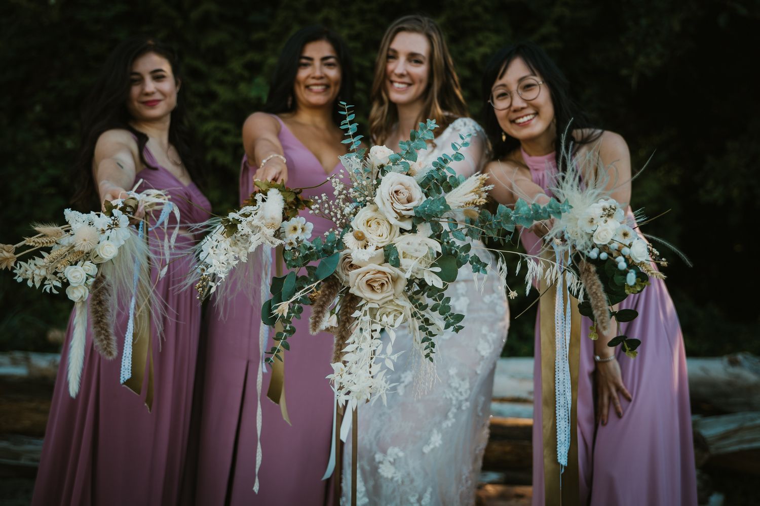 Wedding party holding elegant white and purple floral bouquets outdoors.