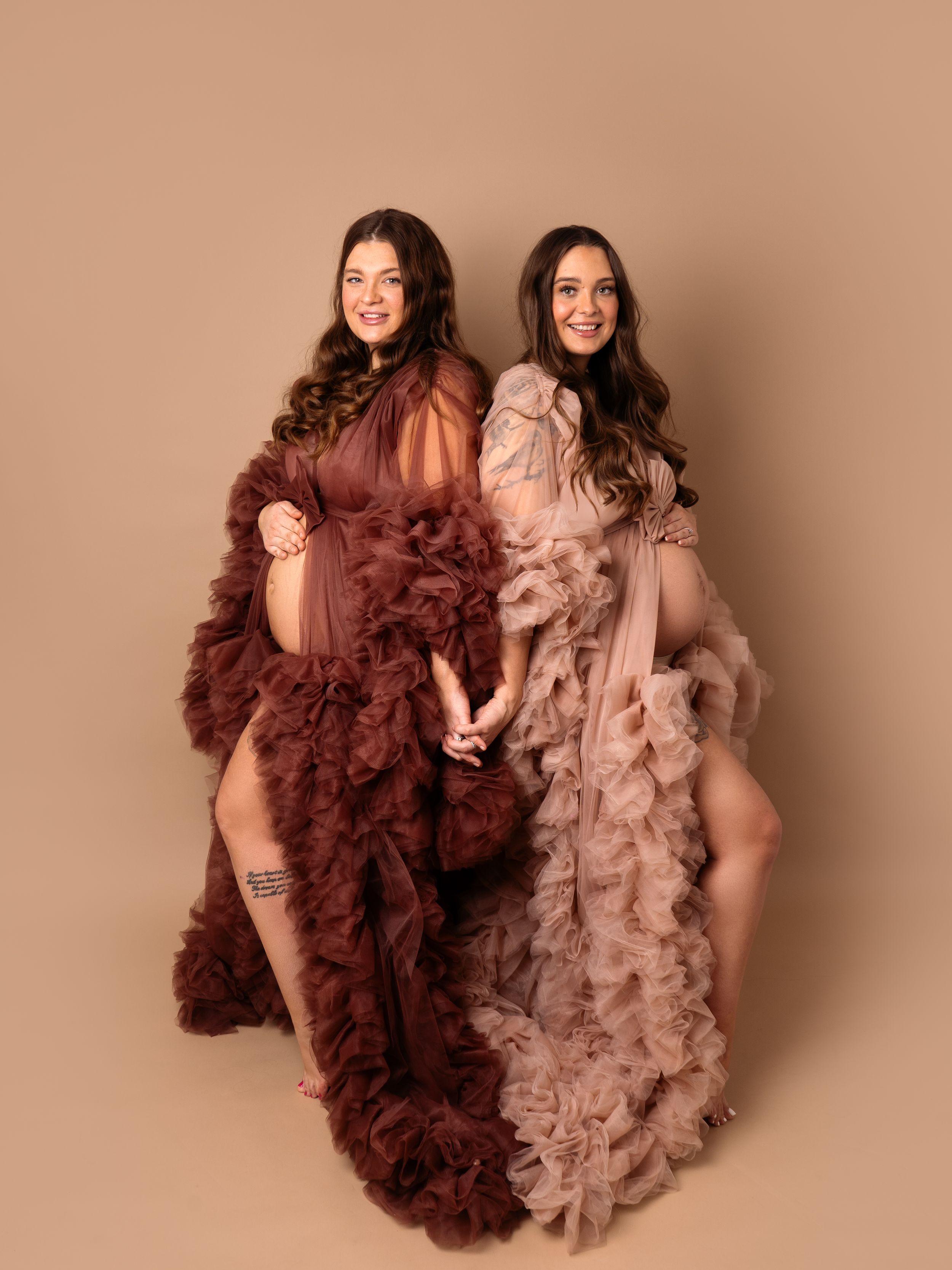two twin sisters posing holding hands and bump in beautiful maternity gowns at maternity photoshoot in Doncaster.