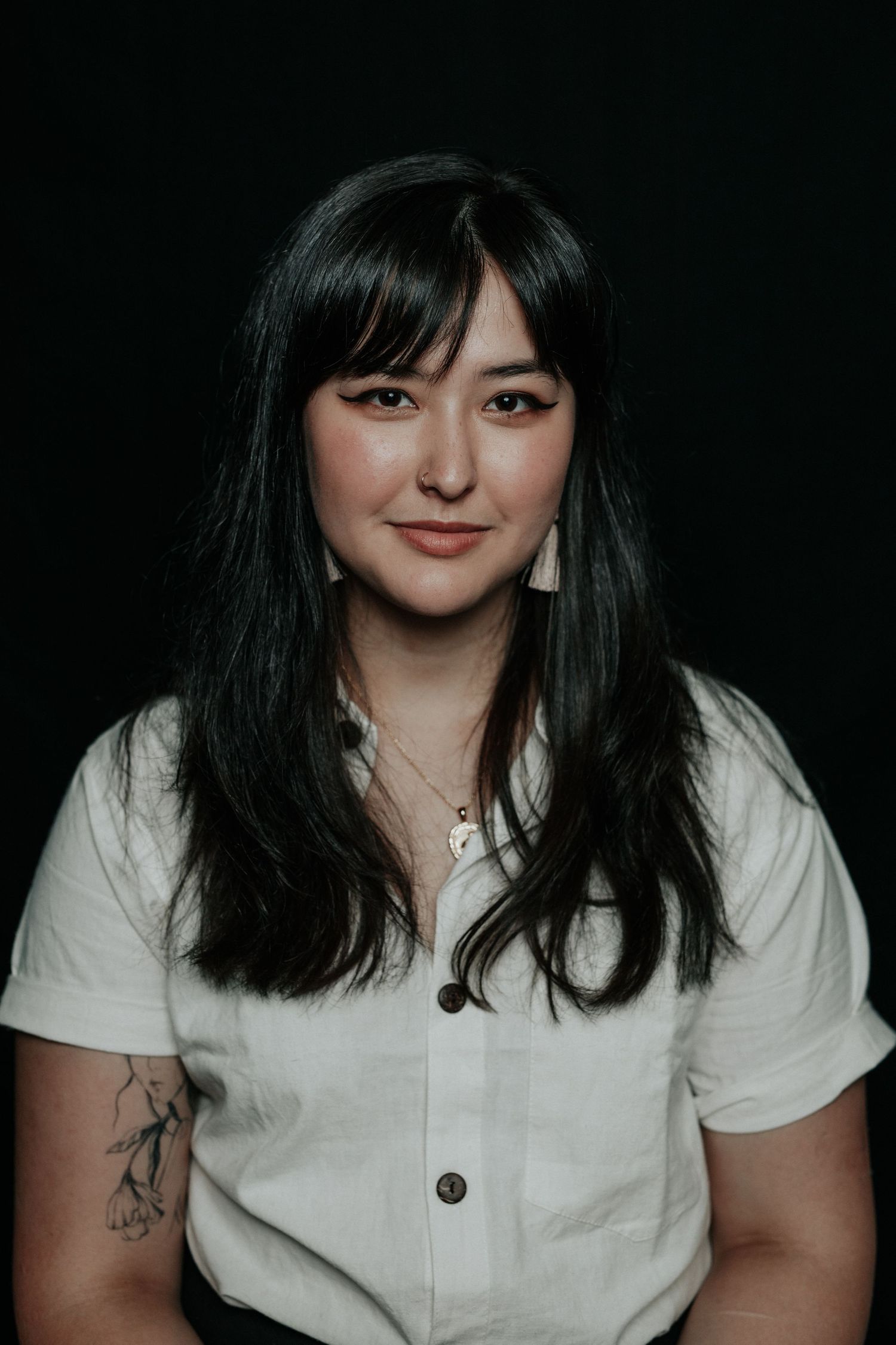 Studio portrait with dark background showcasing long dark hair and white button-up shirt.