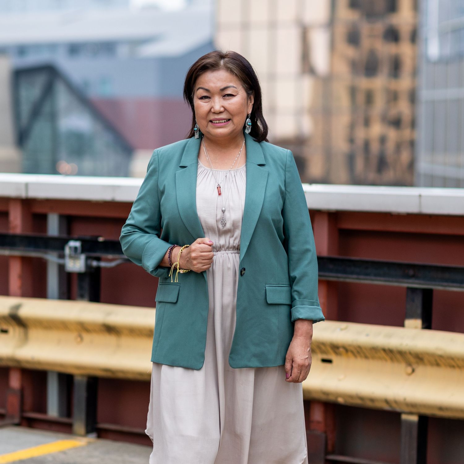 Business portrait in teal blazer and dress on rooftop with city buildings in background.