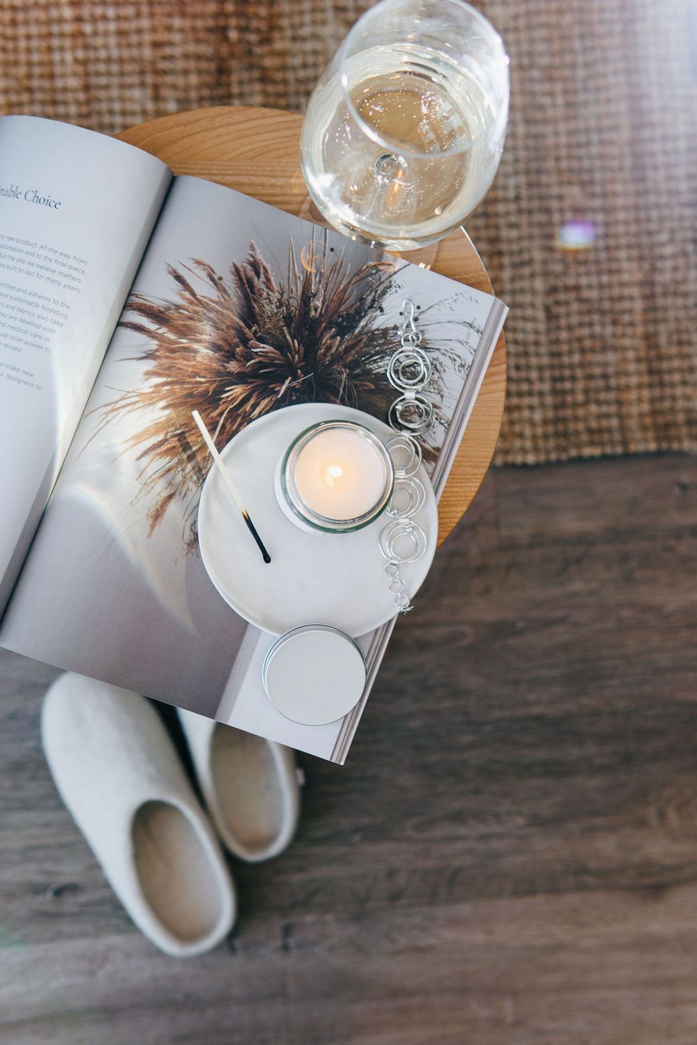 Open book with candle, dried flowers, and wine glass arranged on wooden side table.