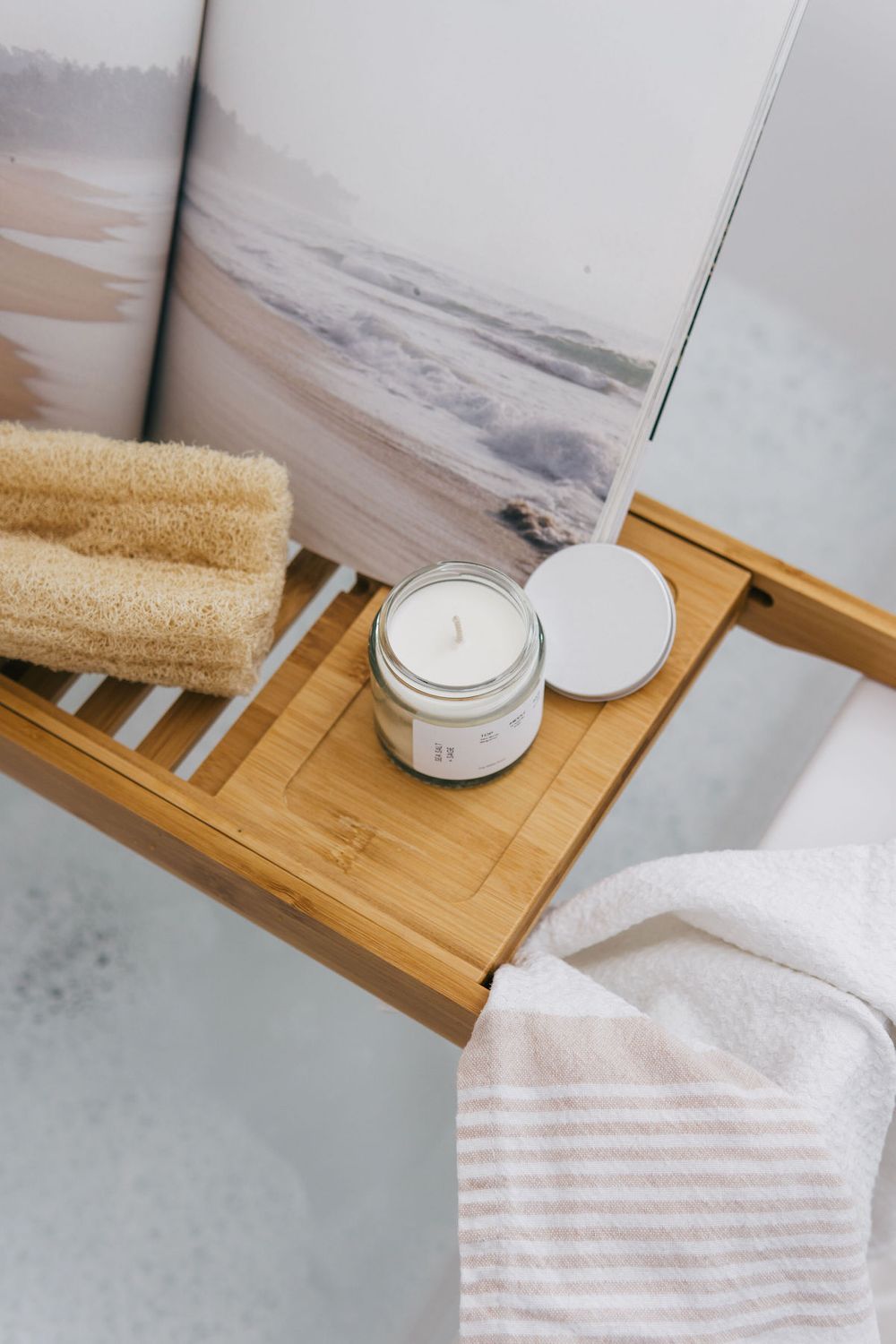 Scented candle on bamboo bath caddy with towel and coastal artwork.