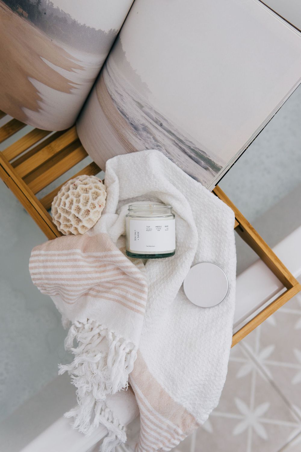 White jar candle with striped towel and bath accessories on wooden caddy tray.