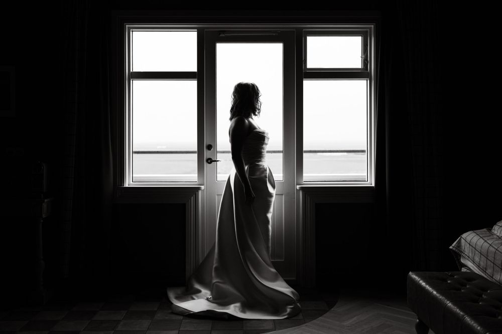 Silhouette of a figure in wedding attire standing by a window in dramatic lighting.