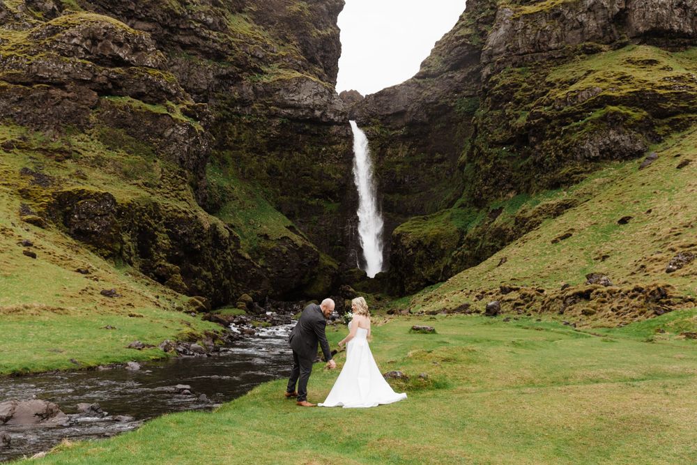 A dramatic waterfall cascades down moss-covered cliffs in Iceland as a couple celebrates their wedding day below.