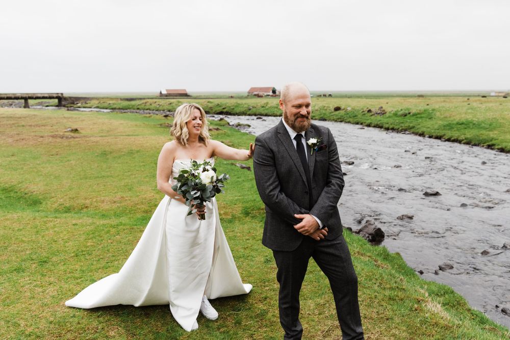 Couple sharing moment during outdoor wedding ceremony by riverside in green landscape.