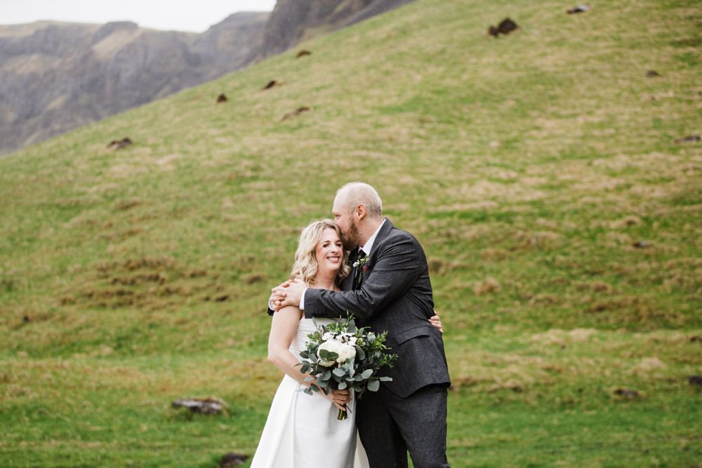A couple shares an intimate moment against a backdrop of rolling green hills in Iceland.