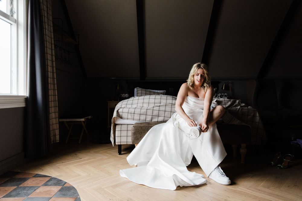 Candid moment of bride in white dress sitting casually in attic room.